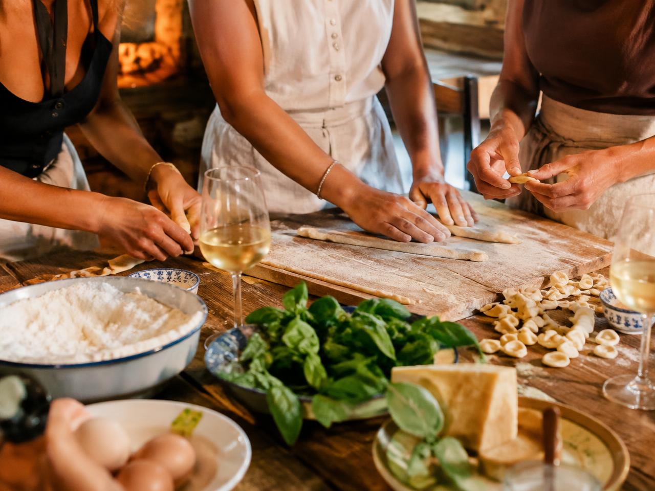 Mani di amiche che preparano orecchiette con basilico e vino bianco